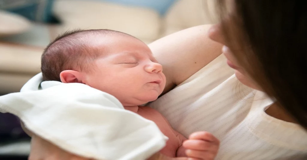 Un bébé dort paisiblement dans les bras de sa mÚre, mettant en valeur l'importance de l'acide folique et grossesse.